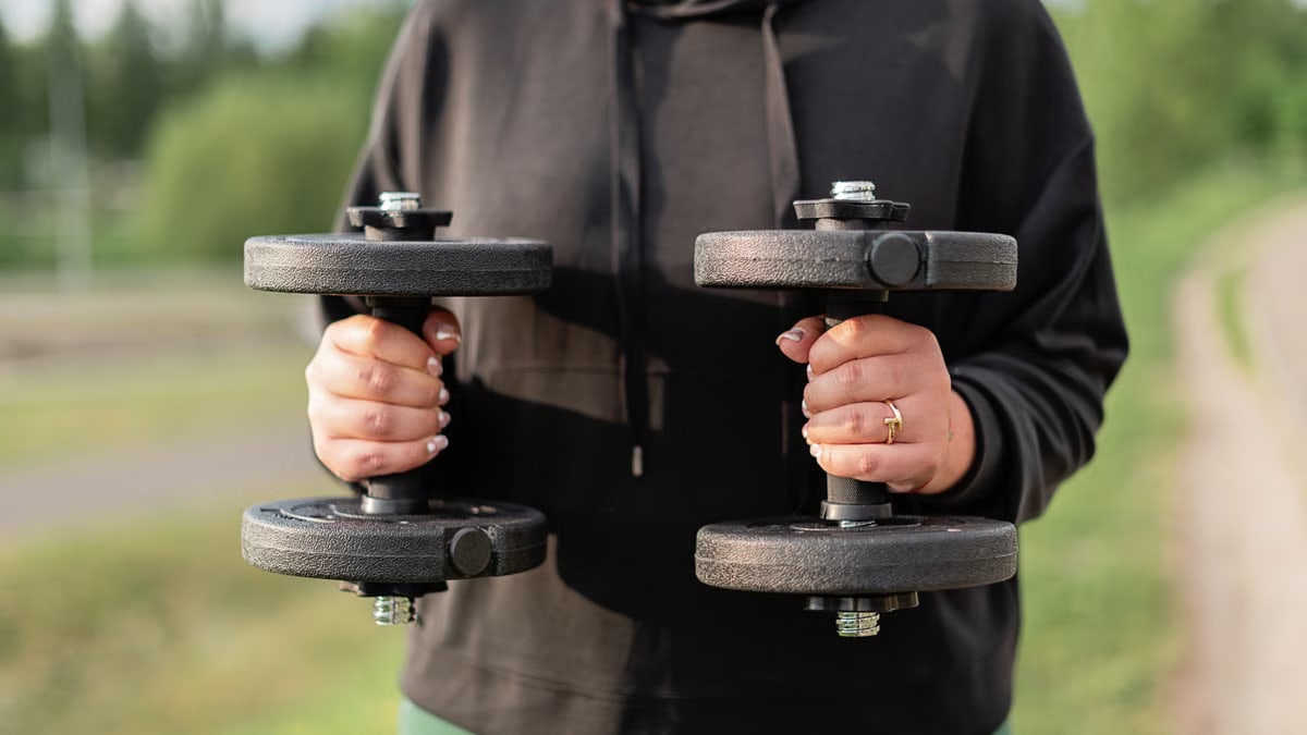 Close-up of a woman holding dumbbells outdoors, focusing on fitness and strength training.